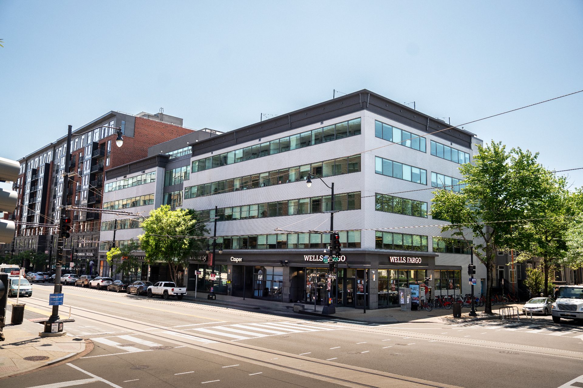 A four-story commercial building on a city street corner with Wells Fargo and Coupe storefronts on the ground floor, surrounded by parked cars and trees.